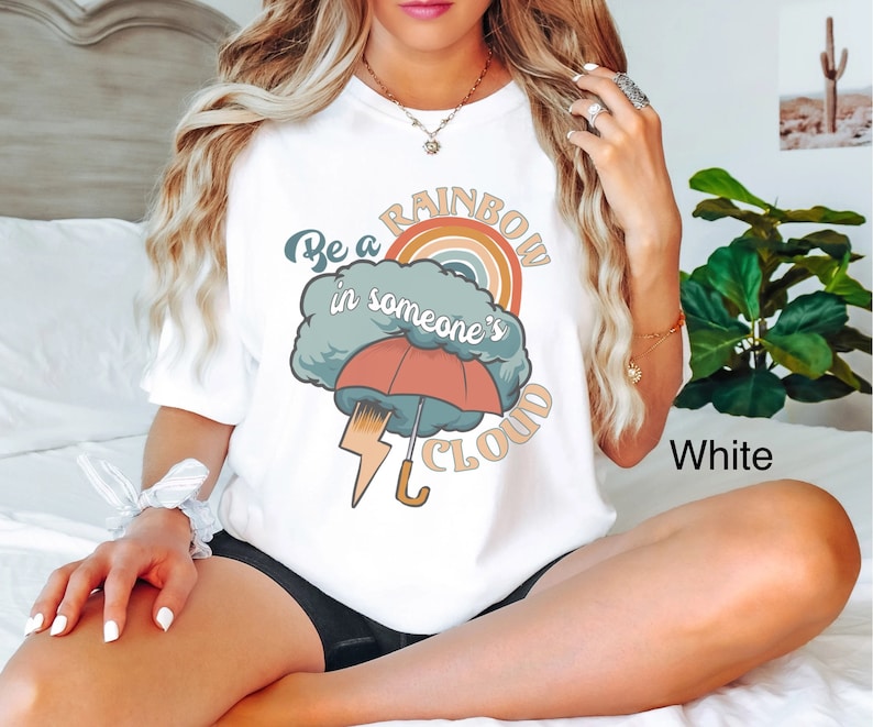 May include: White t-shirt with a graphic of a rainbow in a cloud with the text "Be a rainbow in someone's cloud".