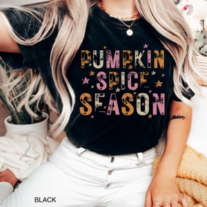 Może przedstawiać: Czarny T-shirt z przetartym nadrukiem, na kt&oacute;rym widnieje napis "Pumpkin Spice Season" w kolorze pomarańczowym, r&oacute;żowym i ż&oacute;łtym z złotymi gwiazdkami.