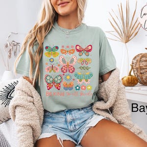 May include: A light blue t-shirt with a graphic of colorful butterflies and the text "Be Kind to all kinds".