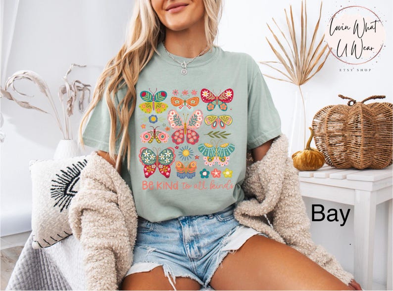 May include: A light blue t-shirt with a graphic of colorful butterflies and the text "Be Kind to all kinds".