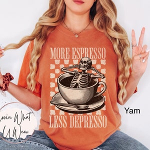 May include: A burnt orange t-shirt with a graphic of a skeleton in a coffee cup. The text on the shirt reads "More Espresso Less Depresso".