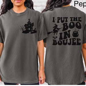 May include: A gray t-shirt with a black graphic of a haunted house on the front and the text "I put the boo in boujee" on the back.