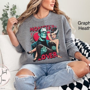 Peut inclure: Un sweat-shirt gris avec un imprim&eacute; graphique de Frankenstein et sa fianc&eacute;e. Le texte sur le sweat-shirt est "Monster Lover".