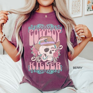 Op de afbeelding: Een maroon t-shirt met een vintage grafisch ontwerp met een schedel die een cowboyhoed en een slang draagt. De tekst "COWBOY KILLER" is gedrukt in een retro lettertype.