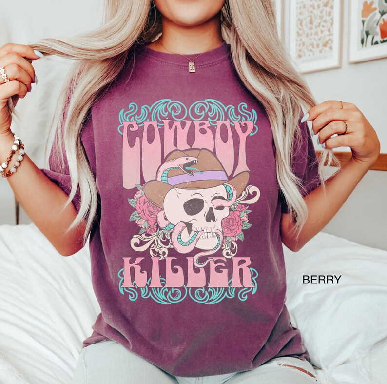Op de afbeelding: Een maroon t-shirt met een vintage grafisch ontwerp met een schedel die een cowboyhoed en een slang draagt. De tekst "COWBOY KILLER" is gedrukt in een retro lettertype.