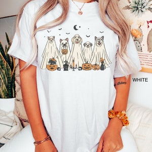 Peut inclure: T-shirt blanc avec un motif de cinq chiens habill&eacute;s en fant&ocirc;mes tenant des citrouilles et des bonbons. Les chiens portent des costumes de fant&ocirc;mes avec une lune croissante et des chauves-souris en arri&egrave;re-plan.