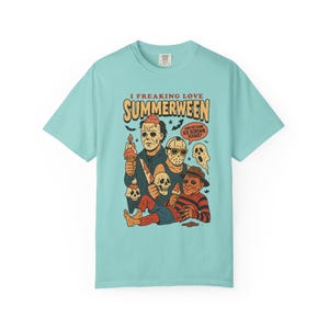 May include: A pale blue t-shirt with a cartoon graphic of horror movie characters enjoying ice cream. The text on the shirt says "I Freaking Love Summerween" and "Can I get some ice cream please?"