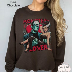 Peut inclure: Un sweat-shirt brun chocolat fonc&eacute; avec un imprim&eacute; graphique de Frankenstein et sa fianc&eacute;e. Le graphique pr&eacute;sente un c&oelig;ur avec le texte "Monster Lover" dans une police de caract&egrave;res vintage.