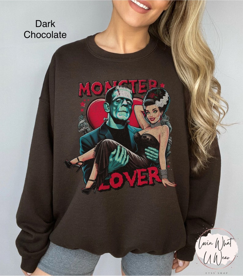 Peut inclure: Un sweat-shirt brun chocolat fonc&eacute; avec un imprim&eacute; graphique de Frankenstein et sa fianc&eacute;e. Le graphique pr&eacute;sente un c&oelig;ur avec le texte "Monster Lover" dans une police de caract&egrave;res vintage.