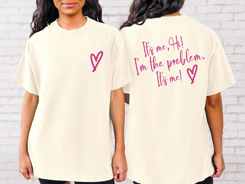 May include: A white t-shirt with a pink heart on the front and the text "It's me, Hi! I'm the problem. It's me!" with a pink heart on the back.