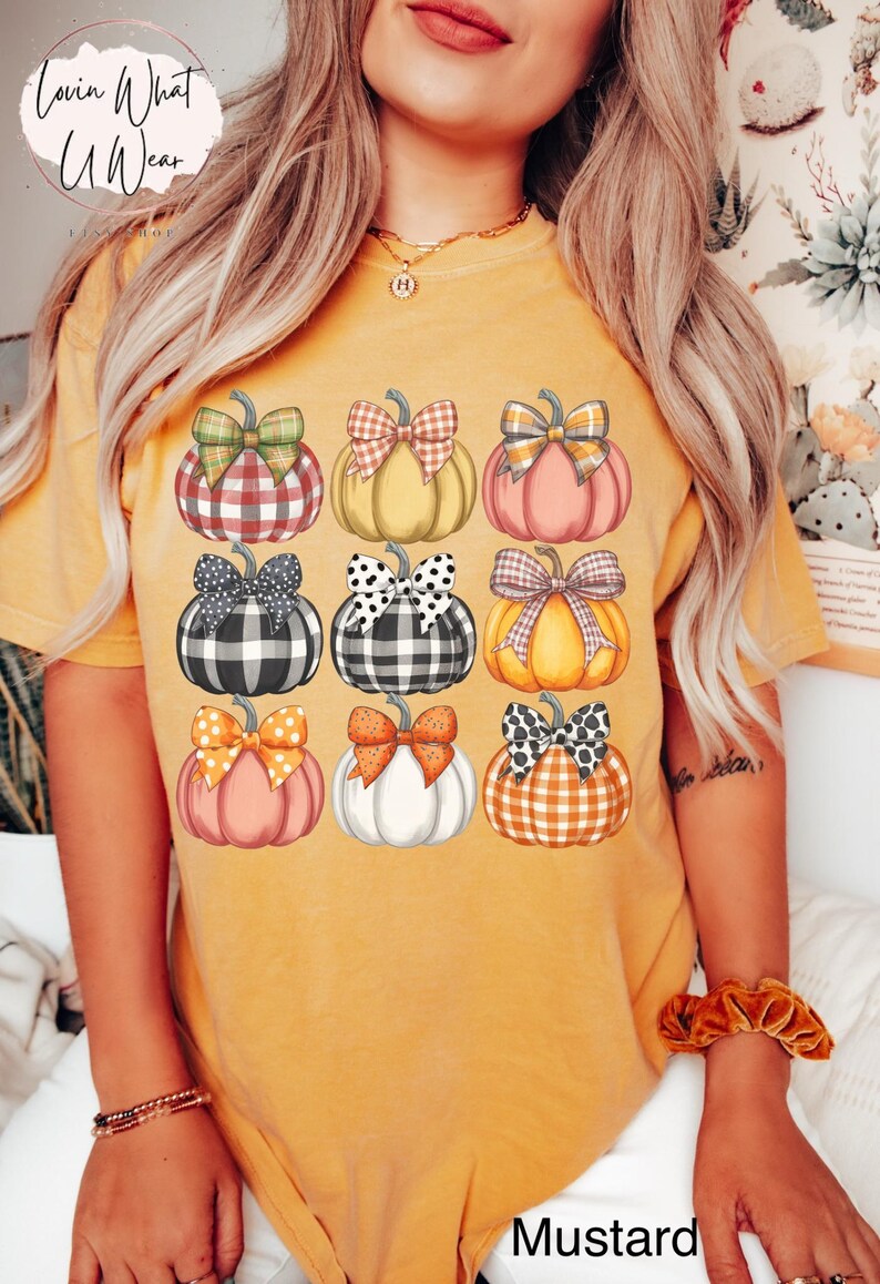 Peut inclure: T-shirt moutarde avec une grille de neuf citrouilles avec des n&oelig;uds &agrave; motifs vari&eacute;s. Les citrouilles sont dans les tons de rose, orange, jaune et blanc. Le texte "Lovin What U Wear" est en haut &agrave; gauche.