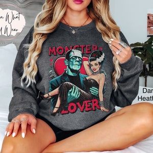 Peut inclure: Sweat-shirt gris chin&eacute; fonc&eacute; avec un imprim&eacute; graphique de Frankenstein et sa fianc&eacute;e. Le graphique comprend le texte "Monster Lover".
