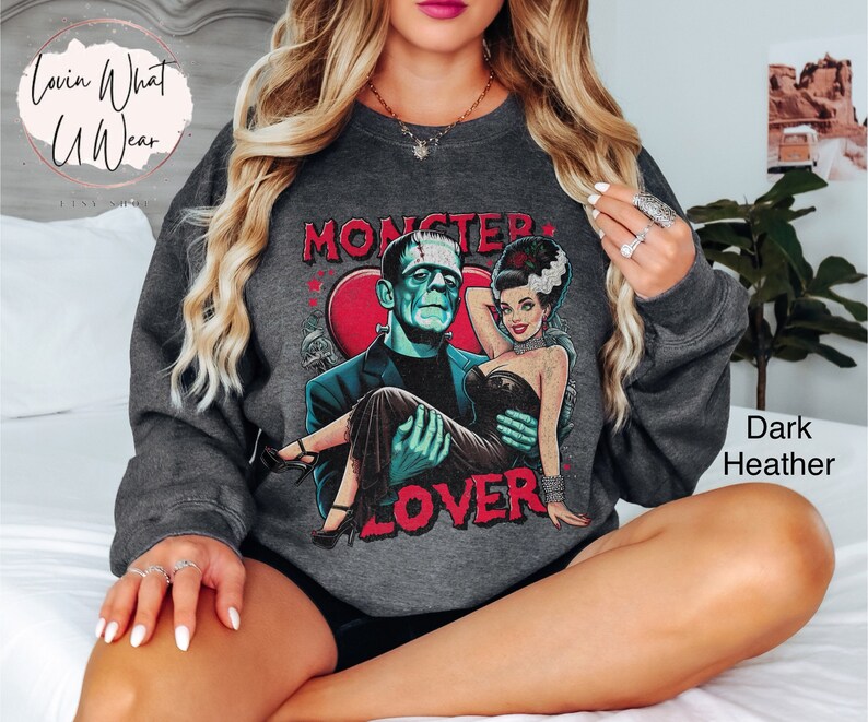 Peut inclure: Sweat-shirt gris chin&eacute; fonc&eacute; avec un imprim&eacute; graphique de Frankenstein et sa fianc&eacute;e. Le graphique comprend le texte "Monster Lover".