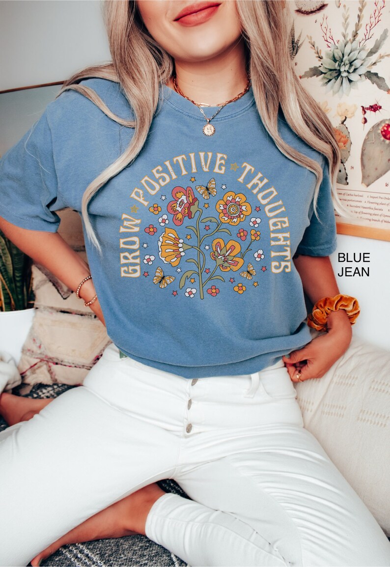 Op de afbeelding: Een blauw t-shirt met een bloemenmotief en de tekst "Grow Positive Thoughts".