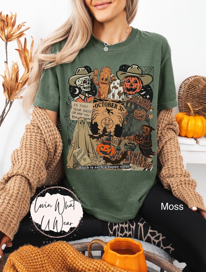 May include: Moss green t-shirt with a Halloween-themed graphic. The design includes a skeleton, jack-o'-lantern, and the text "October 31". Additional text reads "Is that your ghost or are you real here?" and "Halloween will never die".