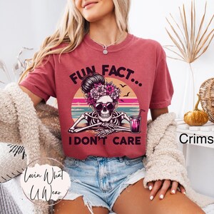 May include: A red t-shirt with a graphic of a skeleton wearing sunglasses and holding a drink. The text "Fun Fact... I don't care" is printed on the shirt.