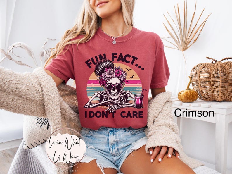 May include: A red t-shirt with a graphic of a skeleton wearing sunglasses and holding a drink. The text "Fun Fact... I don't care" is printed on the shirt.