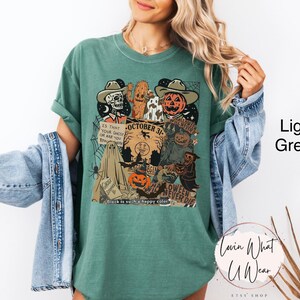 May include: Light green t-shirt with a Halloween-themed graphic. The design includes a skeleton, a pumpkin head, and the text "October 31". The shirt also features a ghost, a spider web, and the phrase "Halloween Never Die".
