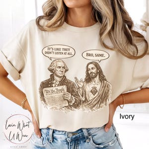 Może przedstawiać: Kremowa koszulka z grafiką George'a Washingtona i Jezusa. Washington trzyma dokument z napisem "We the People". Dymki z napisami "It's like they didn't listen at all" i "Bro, same."