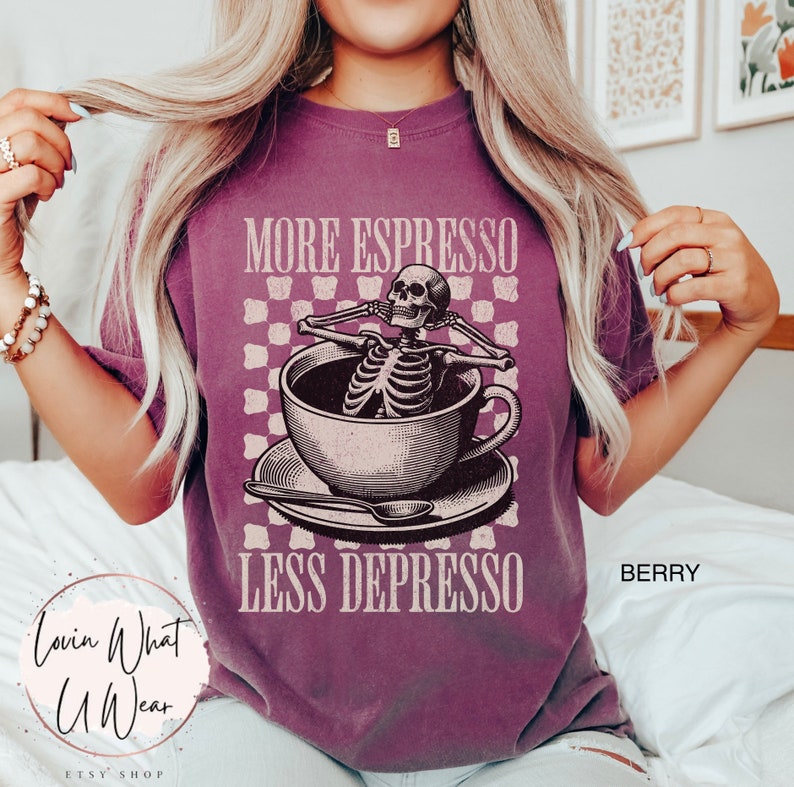 May include: A purple t-shirt with a graphic of a skeleton relaxing in a cup of coffee. The text "More Espresso Less Depresso" is printed on the shirt.