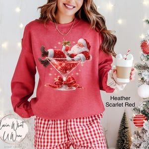 May include: Heather scarlet red sweatshirt with a graphic of Santa Claus relaxing in a martini glass. The image includes a red bow and the text "Lovin What U Wear" and "Heather Scarlet Red".