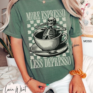 May include: A green t-shirt with a skeleton sitting in a coffee cup. The text on the shirt reads "More Espresso Less Depresso".