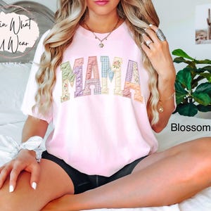 Puede incluir: Una camiseta rosa claro con la palabra "MAMA" en letras de patchwork. Las letras est&aacute;n hechas de varias telas florales y estampadas. La camiseta es parte de la colecci&oacute;n "Blossom" y es de estilo casual.