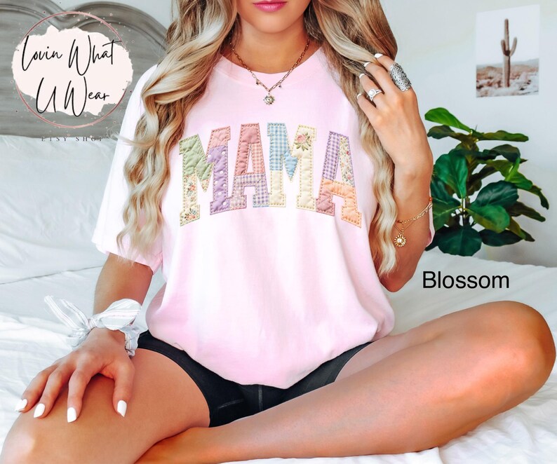 Puede incluir: Una camiseta rosa claro con la palabra "MAMA" en letras de patchwork. Las letras est&aacute;n hechas de varias telas florales y estampadas. La camiseta es parte de la colecci&oacute;n "Blossom" y es de estilo casual.