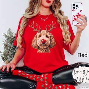 K&ouml;nnte beinhalten: Rotes T-Shirt mit einem Aufdruck eines Hundes, der ein Rentiergeweih und eine rote Nase tr&auml;gt. Der Text "Lovin What U Wear" ist in der rechten unteren Ecke des Bildes zu sehen.