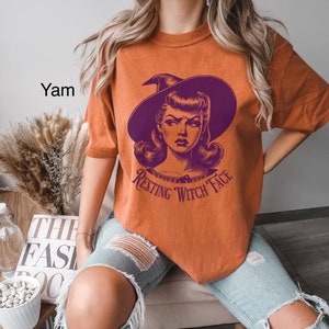 May include: Orange t-shirt with a purple witch graphic and the text "Resting Witch Face".