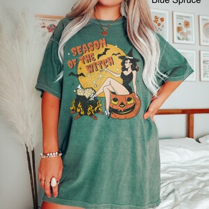Puede incluir: Una camiseta verde con un gr&aacute;fico de estilo vintage de una bruja sentada en una calabaza. El gr&aacute;fico dice "Season of the Witch".