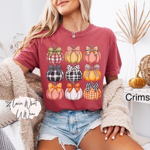 Peut inclure: T-shirt couleur cramoisi avec une grille de neuf citrouilles &agrave; n&oelig;uds &agrave; motifs. Les citrouilles ont diff&eacute;rentes couleurs et motifs, notamment des carreaux, des pois et des couleurs unies. Le t-shirt est associ&eacute; &agrave; un short en jean.