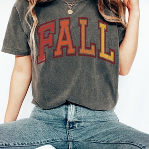 May include: A gray t-shirt with the word "FALL" printed in a vintage style with red, orange, and yellow colors.
