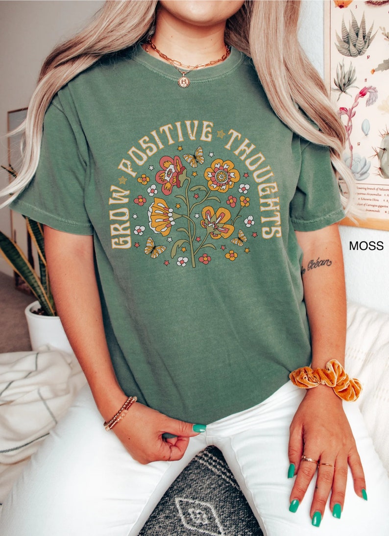 Op de afbeelding: Groen T-shirt met een vintage bloemenontwerp en de tekst "Grow Positive Thoughts".