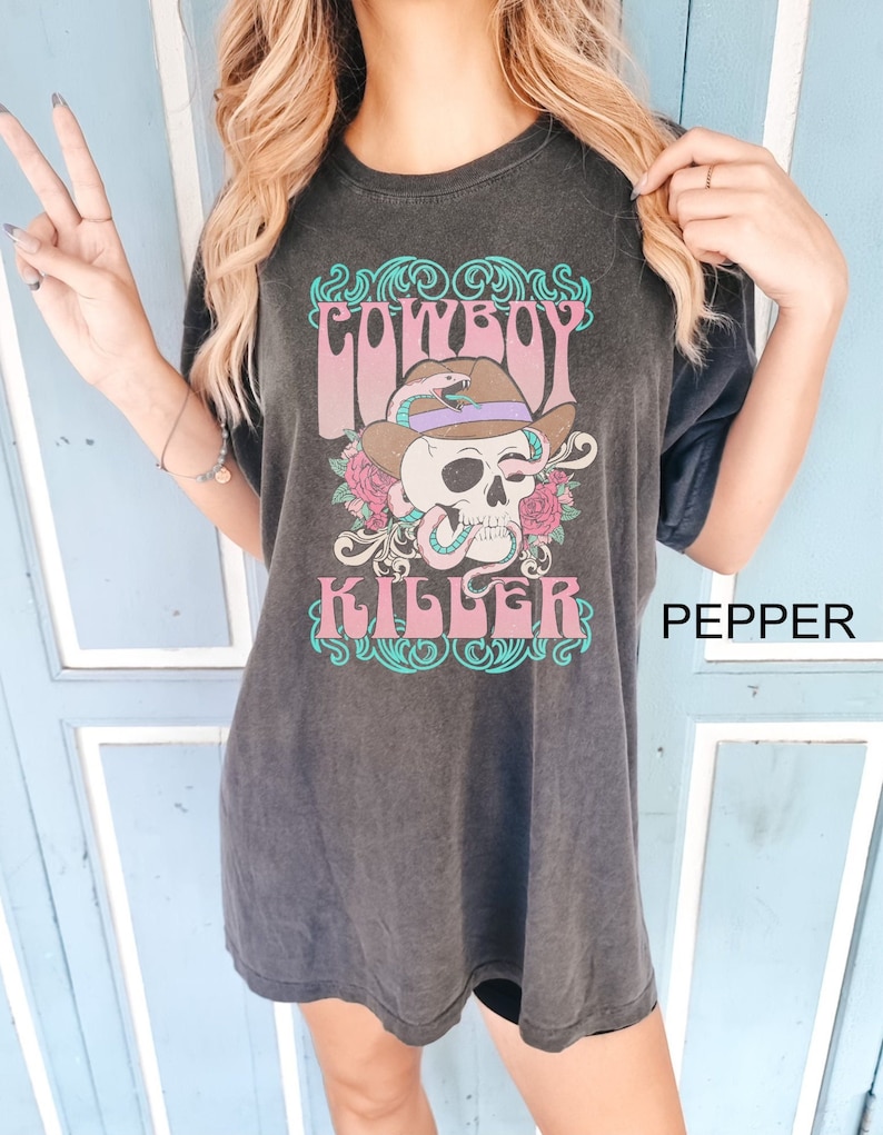 Op de afbeelding: Zwart oversized T-shirt met een grafische print van een schedel die een cowboyhoed en een slang draagt. De tekst "COWBOY KILLER" is op het shirt gedrukt. Het woord "PEPPER" is gedrukt in de rechterbenedenhoek van de afbeelding.