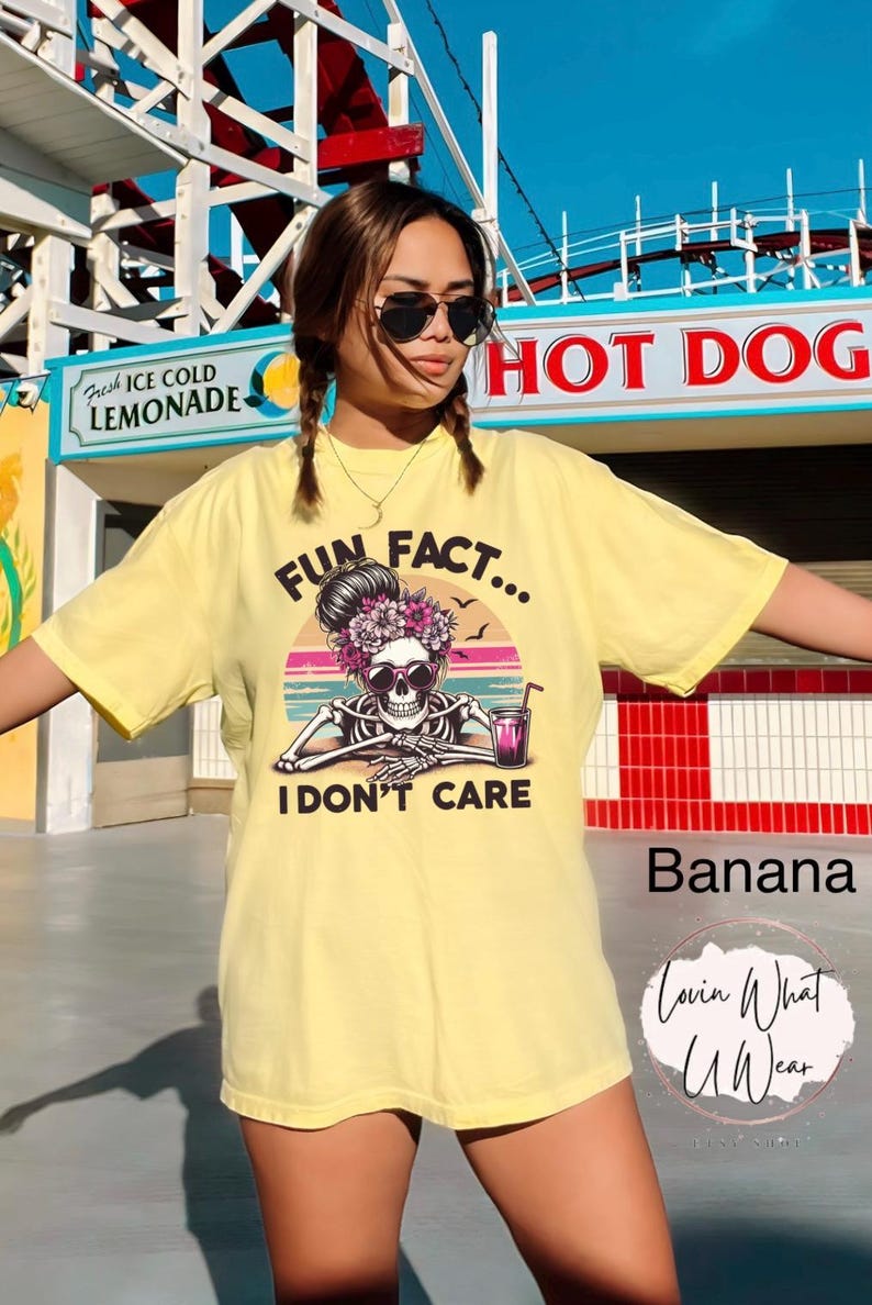 May include: Yellow t-shirt with a skeleton wearing sunglasses and a flower crown. The text on the shirt reads "Fun Fact... I Don't Care".