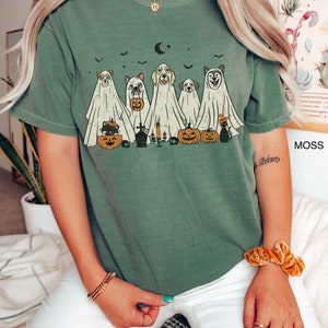 Peut inclure: Un t-shirt vert avec un motif vintage de chiens d&eacute;guis&eacute;s en fant&ocirc;mes pour Halloween. Le motif comprend des citrouilles, un chat et une lune croissante.