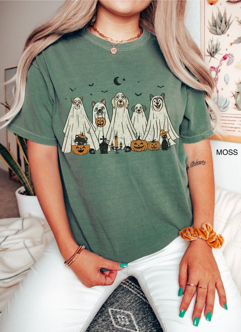 Peut inclure: Un t-shirt vert avec un motif vintage de chiens d&eacute;guis&eacute;s en fant&ocirc;mes pour Halloween. Le motif comprend des citrouilles, un chat et une lune croissante.