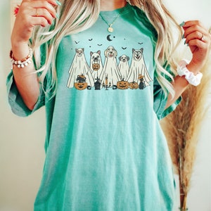 Peut inclure: Un t-shirt bleu turquoise avec un motif de chiens d&eacute;guis&eacute;s en fant&ocirc;mes pour Halloween. Le motif comprend un chat noir, des citrouilles et une lune croissante.