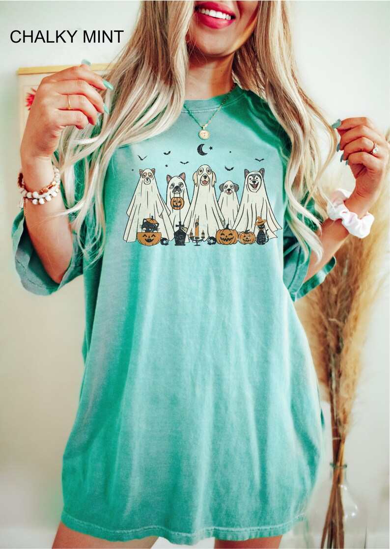 Peut inclure: Un t-shirt bleu turquoise avec un motif de chiens d&eacute;guis&eacute;s en fant&ocirc;mes pour Halloween. Le motif comprend un chat noir, des citrouilles et une lune croissante.