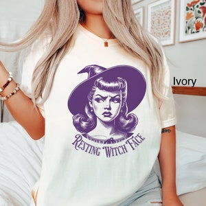 May include: A white t-shirt with a purple illustration of a witch with the text "Resting Witch Face".