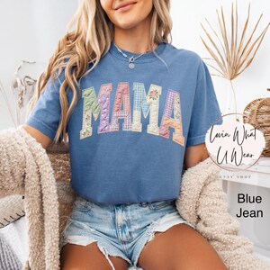 Puede incluir: Camiseta azul vaquero con la palabra "MAMA" en letras de patchwork. Las letras son de varios colores y patrones pastel. La camiseta es de manga corta y tiene cuello redondo.
