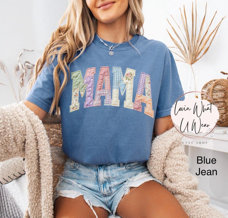 Puede incluir: Camiseta azul vaquero con la palabra "MAMA" en letras de patchwork. Las letras son de varios colores y patrones pastel. La camiseta es de manga corta y tiene cuello redondo.