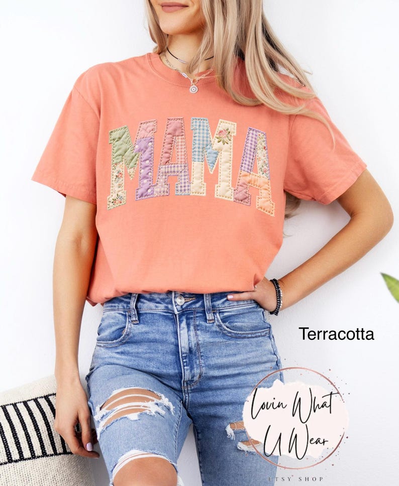 Puede incluir: Camiseta color terracota con la palabra "MAMA" en letras de patchwork. Las letras est&aacute;n hechas de varias telas florales y estampadas. La camiseta se combina con pantalones cortos de mezclilla azules. El texto "Terracota" es visible.