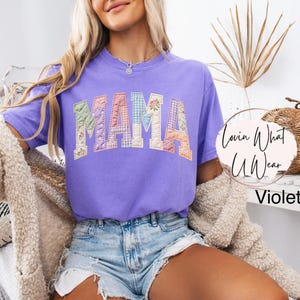 Puede incluir: Una camiseta violeta con la palabra "MAMA" en letras de patchwork. Las letras est&aacute;n hechas de varias telas florales y estampadas. La camiseta forma parte de la colecci&oacute;n "Lovin What U Wear".