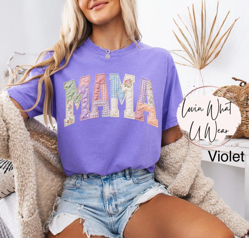 Puede incluir: Una camiseta violeta con la palabra "MAMA" en letras de patchwork. Las letras est&aacute;n hechas de varias telas florales y estampadas. La camiseta forma parte de la colecci&oacute;n "Lovin What U Wear".