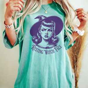 May include: A teal green t-shirt with a vintage illustration of a witch with the text "Resting Witch Face" printed on the front.