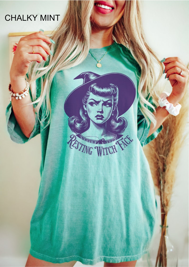 May include: A teal green t-shirt with a vintage illustration of a witch with the text "Resting Witch Face" printed on the front.