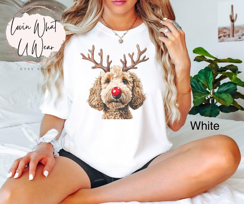 K&ouml;nnte beinhalten: Wei&szlig;es T-Shirt mit einem braunen Hund mit Rentiergeweih und roter Nase. Der Text "White" ist in der rechten unteren Ecke des Bildes sichtbar.