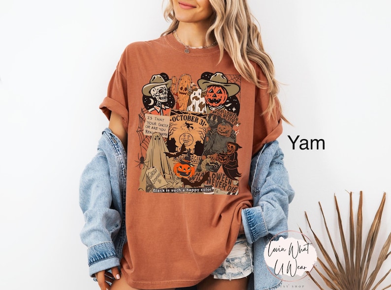 May include: A yam-colored t-shirt with a Halloween-themed graphic. The design includes a skeleton, a pumpkin, a ghost, and the text "October 31". The phrase "Black is such a happy color" is also visible.